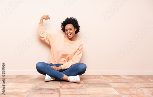 African american woman sitting on the floor doing strong gesture