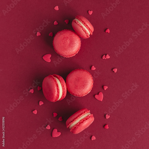 Tasty french macaroons on a dark red background, decorated with sweet hearts. Concept for Valentine's Day.
