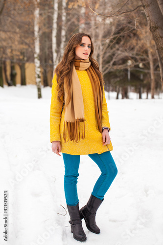 Young beautiful woman in yellow coat walking winter park
