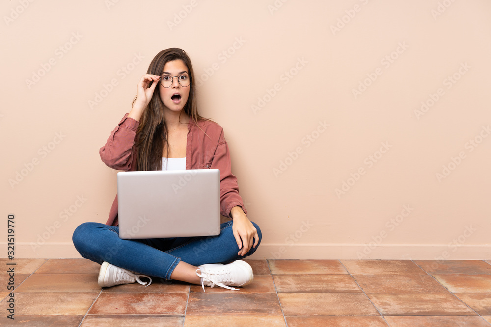Teenager student girl sitting on the floor with a laptop with glasses and surprised Teenager student girl sitting on the floor with a laptop with glasses and surprised