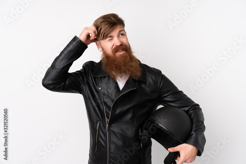 Redhead man with long beard holding a motorcycle helmet over isolated white background having doubts and with confuse face expression