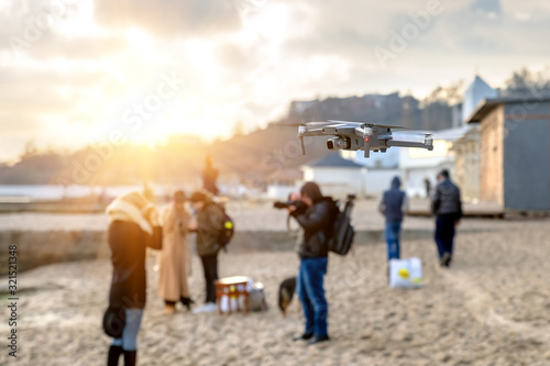 Shooting video and photo of drones closeup on sky background and people walking along the beach near the sea