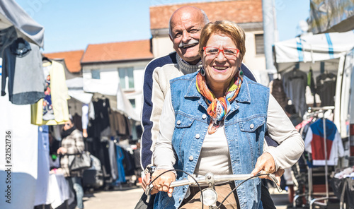 Happy senior couple having fun on bicycle at city market - Active playful elderly concept riding bike at retirement time - Everyday joy lifestyle without age limitation on warm bright sunny day filter © Mirko Vitali