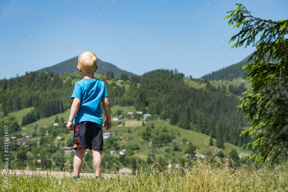 Little blond boy stands on mountains background. Travel with children. Back view Little blond boy stands on mountains background. Travel with children. Back view