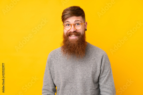 Redhead man with long beard over isolated yellow background with glasses and happy