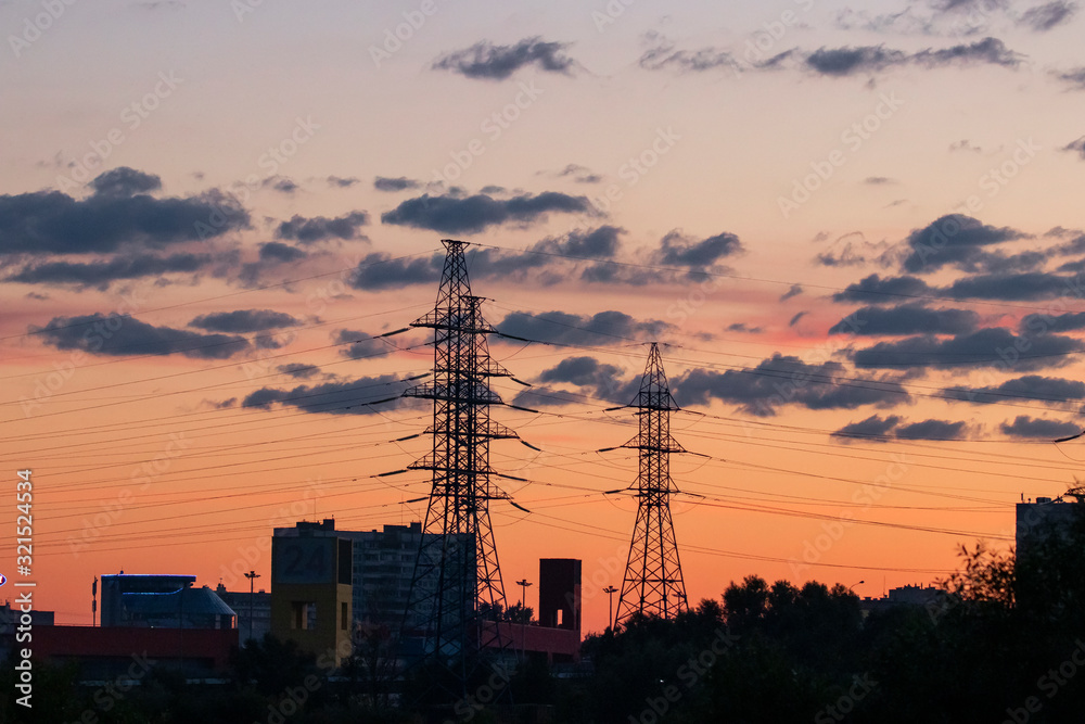 Power lines on city background and orange sunset sky. Industrial city concept