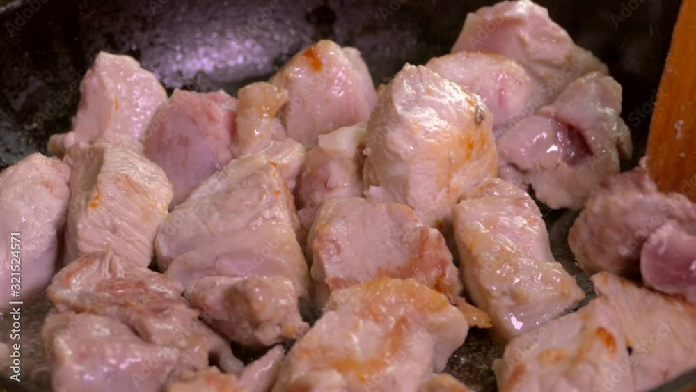 Fresh meat is fried in a pan. Pieces of pork are mixed with a kitchen spatula. Fresh meat is fried in a pan. Pieces of pork are mixed with a kitchen spatula.