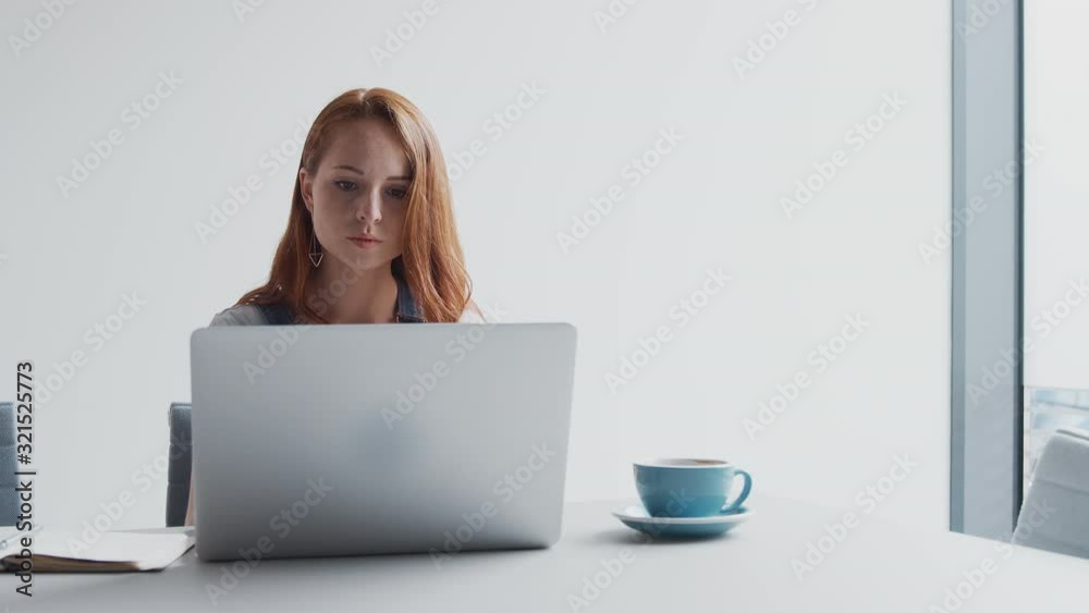 Casually Dressed Young Businesswoman Working On Laptop In Modern Office Taking Call On Mobile Phone Casually Dressed Young Businesswoman Working On Laptop In Modern Office Taking Call On Mobile Phone