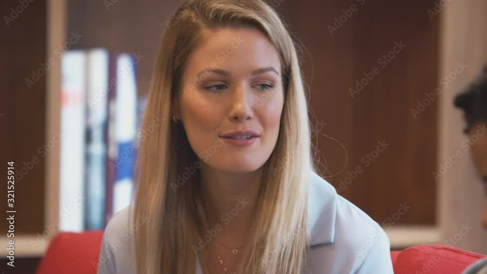 Group Of Young Businesswomen Sitting On Sofas In Open Plan Workspace Having Discussion Group Of Young Businesswomen Sitting On Sofas In Open Plan Workspace Having Discussion