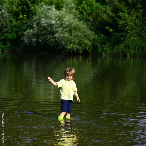 Young boy standing in river with fishing rod on sunny day. Cute boy is fishing in the river in the summer. Cute little boy fishing on pond.