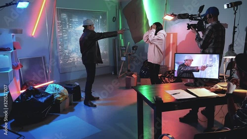 Backstage of thriller film shooting: black man trying to shoot young black woman. Cameraman and film producer are in the background.