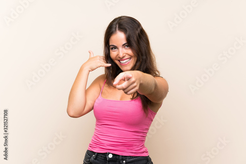 Young woman over isolated white background making phone gesture and pointing front