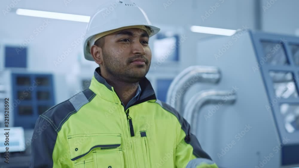 Industry 4 Factory: Portrait of a Modern Worker Wearing Safety Jacket Puts on Hard Hat and Walks Through Contemporary Industrial Workshop where Professionals are Working and Programming CNC Machinery Industry 4 Factory: Portrait of a Modern Worker Wearing Safety Jacket Puts on Hard Hat and Walks Through Contemporary Industrial Workshop where Professionals are Working and Programming CNC Machinery