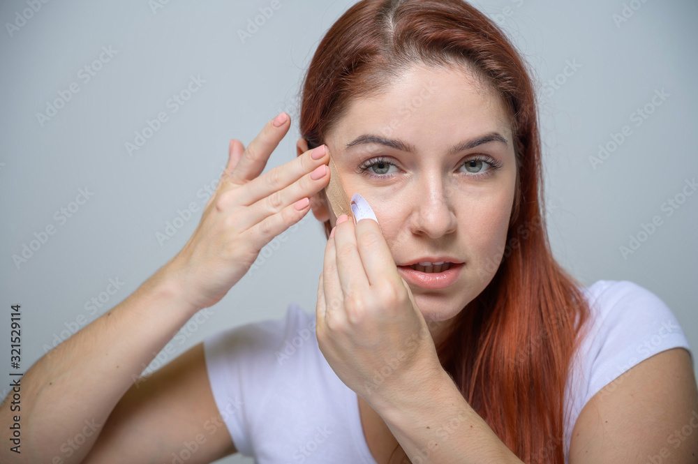 Portrait Beautiful Red-haired Woman with Kinesiology Facelift Tape. Girl beautician puts on face kinesio tape for facelift. Portrait Beautiful Red-haired Woman with Kinesiology Facelift Tape. Girl beautician puts on face kinesio tape for facelift.