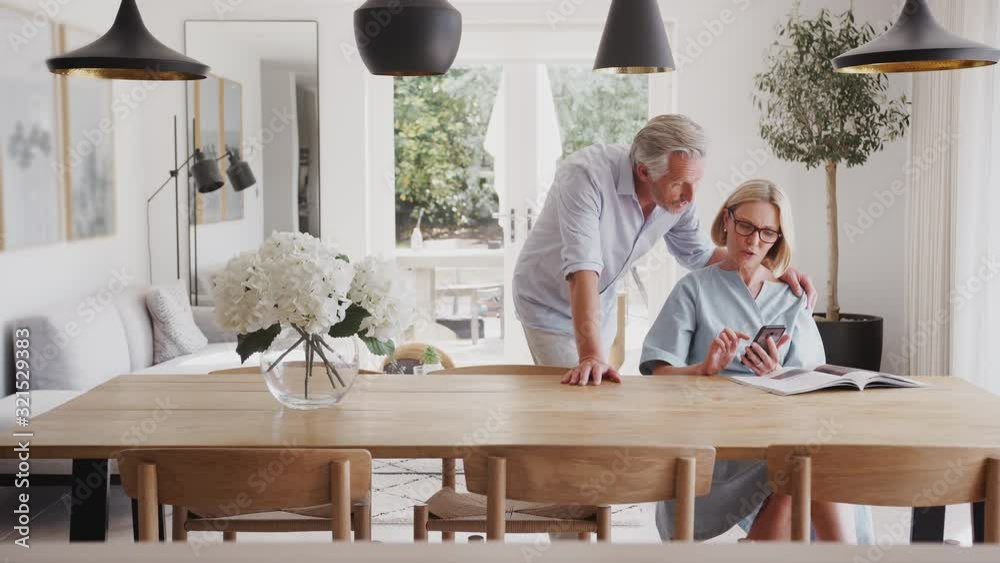 Senior Couple In Dining Room At Home Looking At And Mobile Phone Together Senior Couple In Dining Room At Home Looking At And Mobile Phone Together