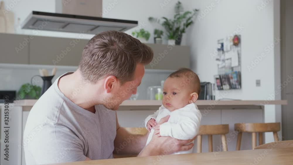 Loving Father Holding 3 Month Old Baby Daughter In Kitchen At Home Playing Game Loving Father Holding 3 Month Old Baby Daughter In Kitchen At Home Playing Game
