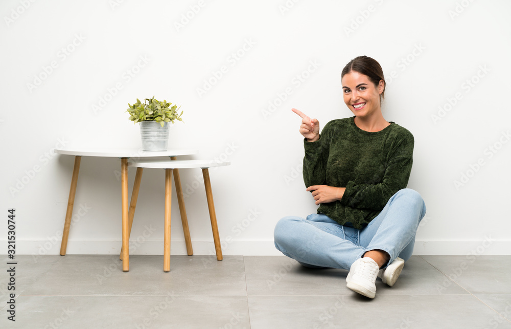 Young woman sitting on the floor pointing finger to the side Young woman sitting on the floor pointing finger to the side