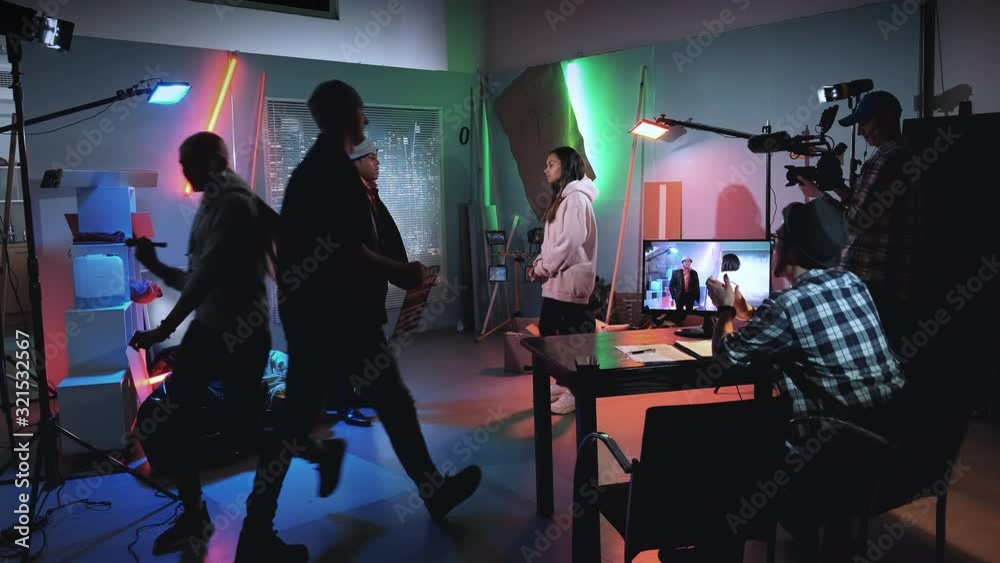 Film crew working on movie production. Make-up artist applying make-up on black actress, producer assistant gives action with movie clapper board.