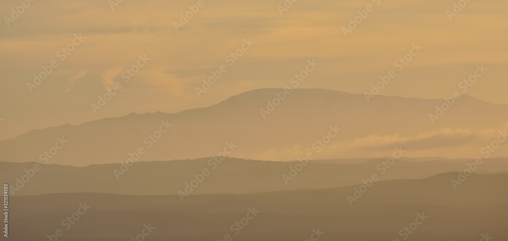 Silhouette of distant mountains between mist at sunset
