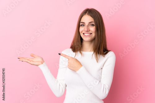 Young woman over isolated pink background holding copyspace imaginary on the palm to insert an ad