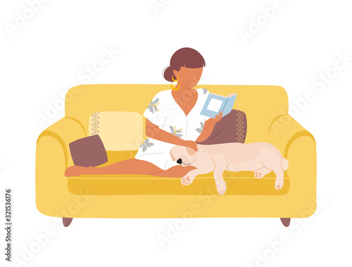 Woman on yellow sofa reading book and petting dog