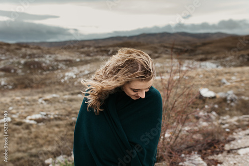 Portrait of young woman with hair blowing in the wind. She is wearing a leather jacket with a blurred nature and road in background. Wanderlust autumn travel, atmospheric moment. 