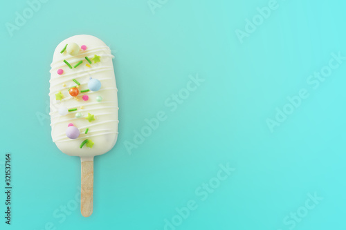 cake - popsicle in white chocolate glaze and colored sprinkles on a blue background. space for text..