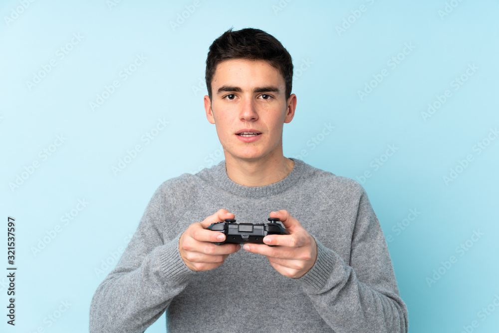 Teenager caucasian man playing with a video game controller isolated on blue background Teenager caucasian man playing with a video game controller isolated on blue background