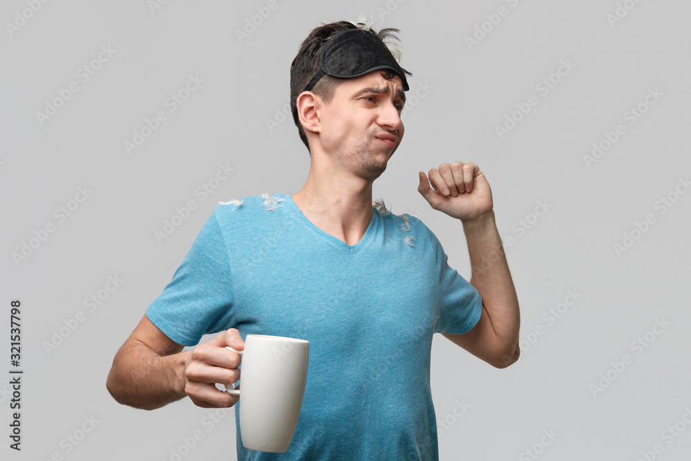 Young brunet man with sleep mask holding white cup with coffee isolated over grey background. Young brunet man with sleep mask holding white cup with coffee isolated over grey background.