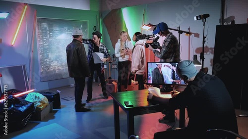 Film shooting backstage: film director showing african star how to threaten a gun in movie scene while all crew preparing for a new take.
