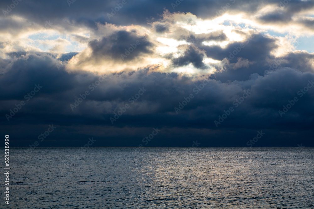 Obraz premium blue dark stormy clouds above the sea, the sunlight breaks through the clouds