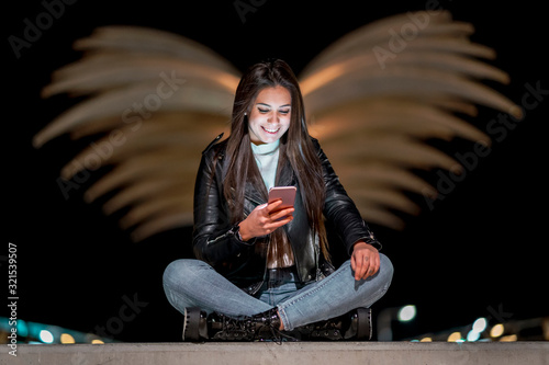 Portrait of happy teenage girl looking at smartphone at night photo