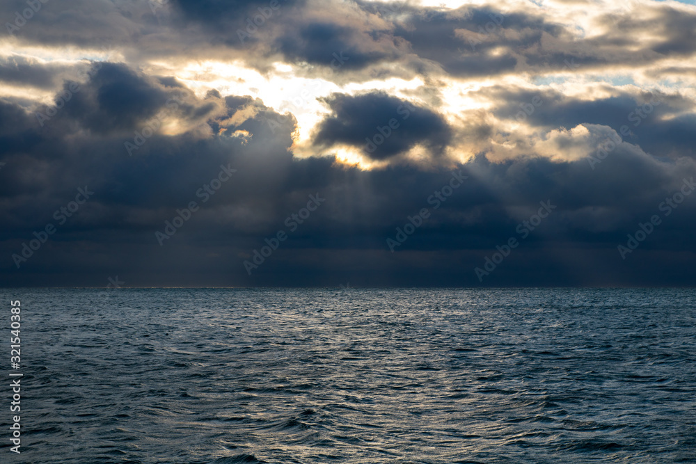 blue dark stormy clouds above the sea, the sun rays breaks through the clouds
