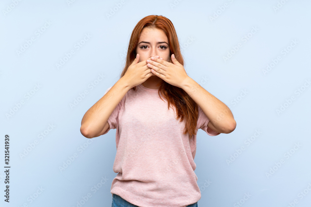 Teenager redhead girl over isolated blue background covering mouth with hands Teenager redhead girl over isolated blue background covering mouth with hands
