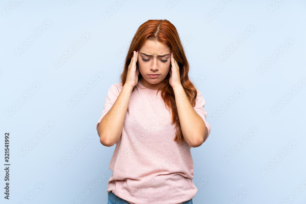Teenager redhead girl over isolated blue background with headache Teenager redhead girl over isolated blue background with headache