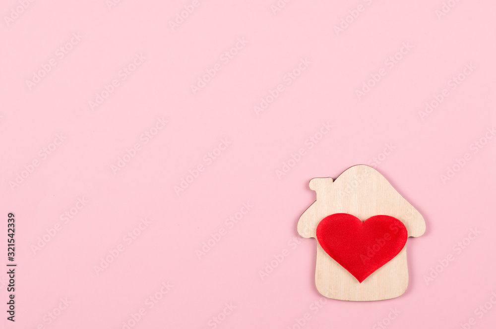 Wooden small house, a red heart on it on a pink background. The concept of love, happiness in your home. Real estate, mortgage