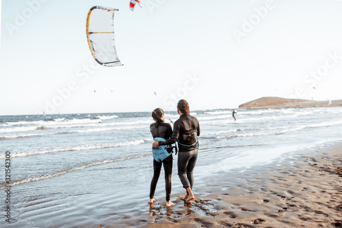 Fotografi Couple of kitesurfers catching airflow with kite on the beach, view from the bac