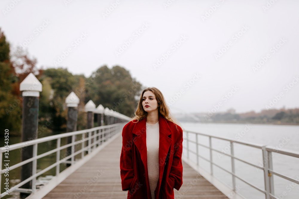 Portrait of young woman wearing red coat on a bridge during rainy day