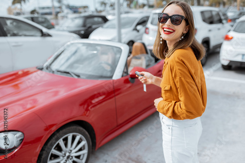 Portrait of a beautiful young woman standing with keys near the red cabriolet at the car parking outdoors. Concept of a happy car buying or renting © rh2010