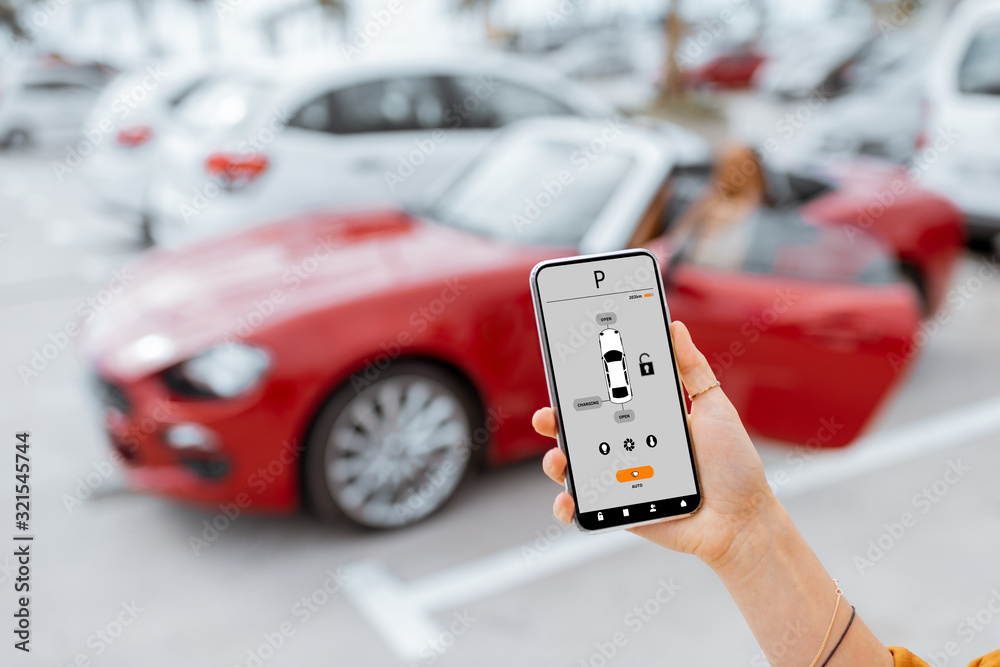 Woman controlling car with mobile application while standing near the vehicle at the parking, close-up view on the smartphone with app interface