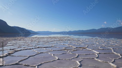 Badwater Basin at Sunny Day. Salt Crust Formations with Water and Blue Sky. Death Valley National Park. California, USA. Panning