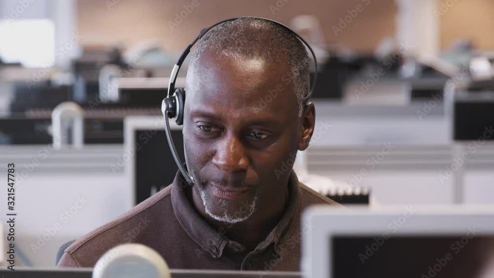 Mature Businessman Wearing Telephone Headset Talking To Caller In Customer Services Department