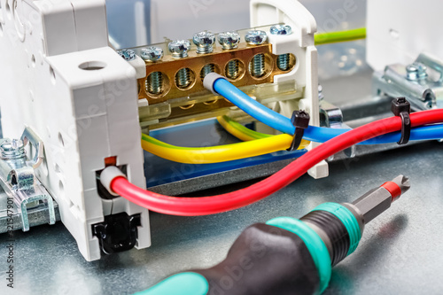 Connected by colored wires electrical equipment against screwdriver with colored plastic handle close-up. Electrical panel assembling