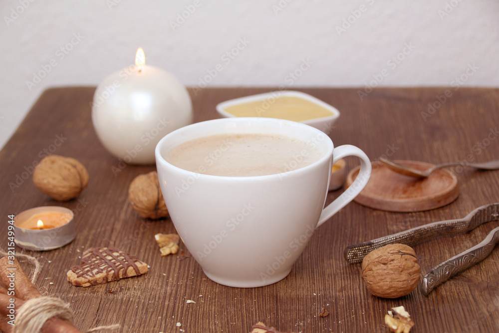 Fototapeta premium white cup with cappuccino coffee stands on a wooden table, honey, nuts, a candle burns