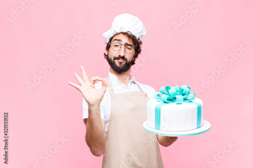 Foto young crazy baker man holding a cake against pink wall