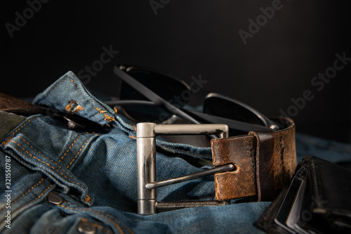 Men's accessories, fashion trends, jeans, a leather belt, an ajar wallet, accidentally lie on a black background with blurred depth of field, close-up. Emphasizes the masculinity of a real man.