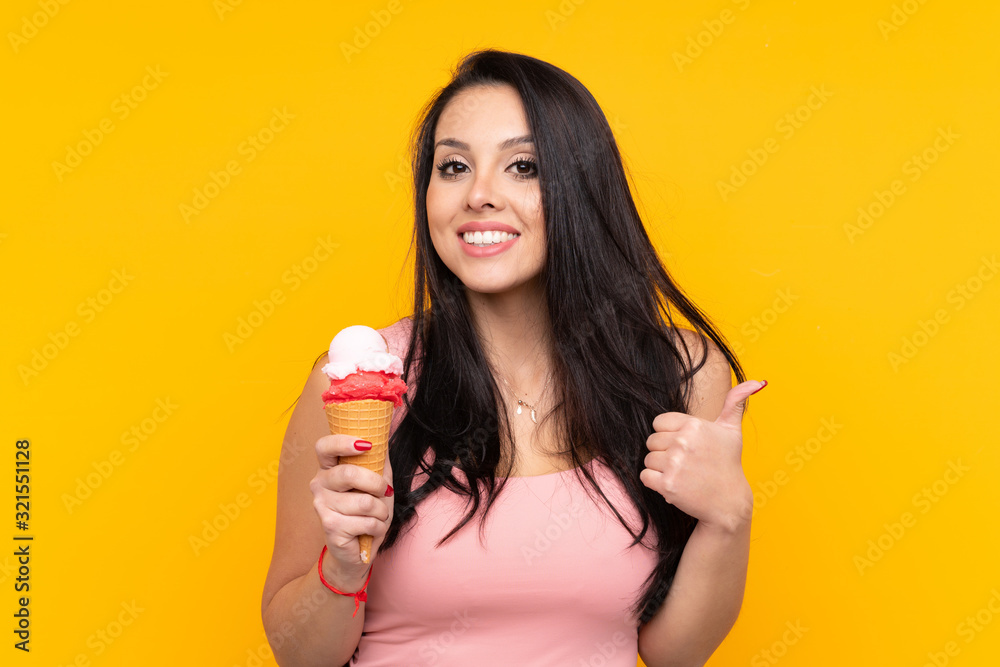 Young Colombian girl holding an cornet ice cream over isolated yellow background with thumbs up because something good has happened Young Colombian girl holding an cornet ice cream over isolated yellow background with thumbs up because something good has happened