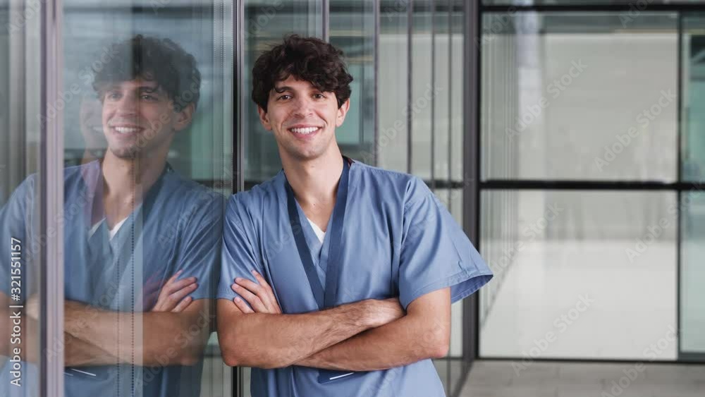 Portrait Of Male Doctor Wearing Scrubs Standing In Modern Hospital Building Portrait Of Male Doctor Wearing Scrubs Standing In Modern Hospital Building