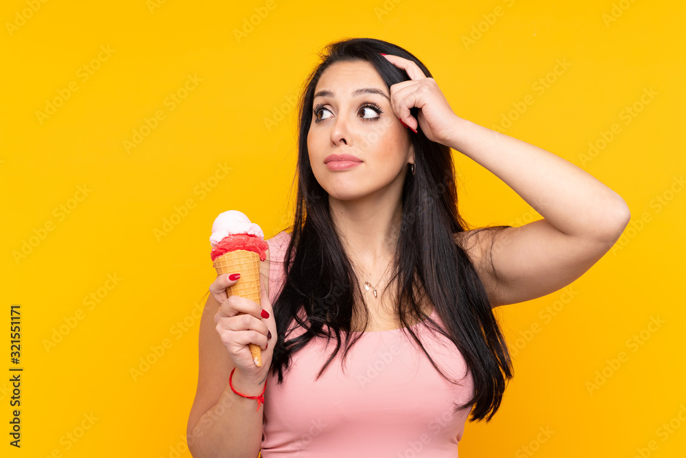 Young Colombian girl holding an cornet ice cream over isolated yellow background having doubts and with confuse face expression Young Colombian girl holding an cornet ice cream over isolated yellow background having doubts and with confuse face expression