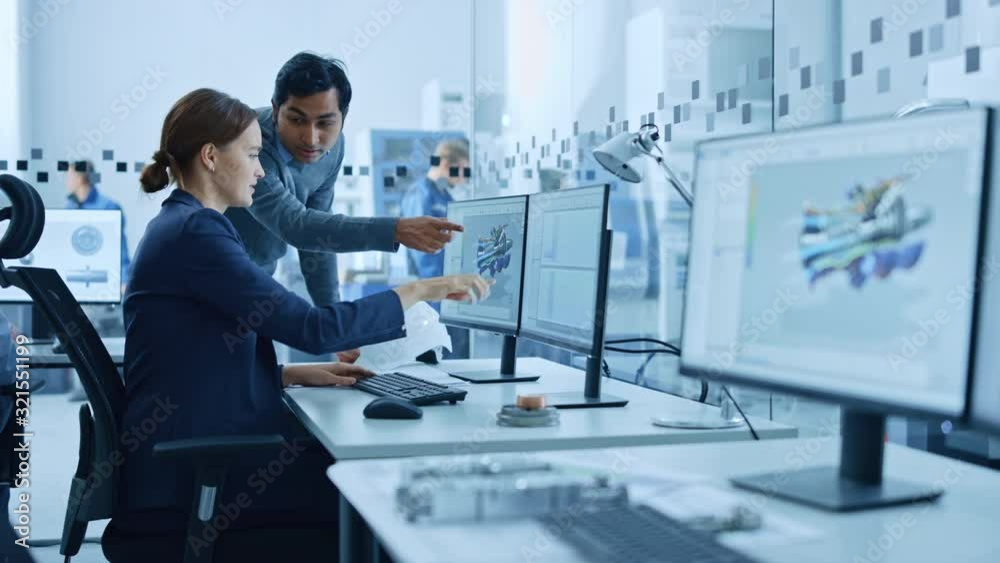Inside Factory Office: Male Project Supervisor Talks to a Female Industrial Engineer who Works on Computer, Talk. In Workshop: Professional Workers Use High-Tech Industry 4 CNC Machinery, Robot Arm.